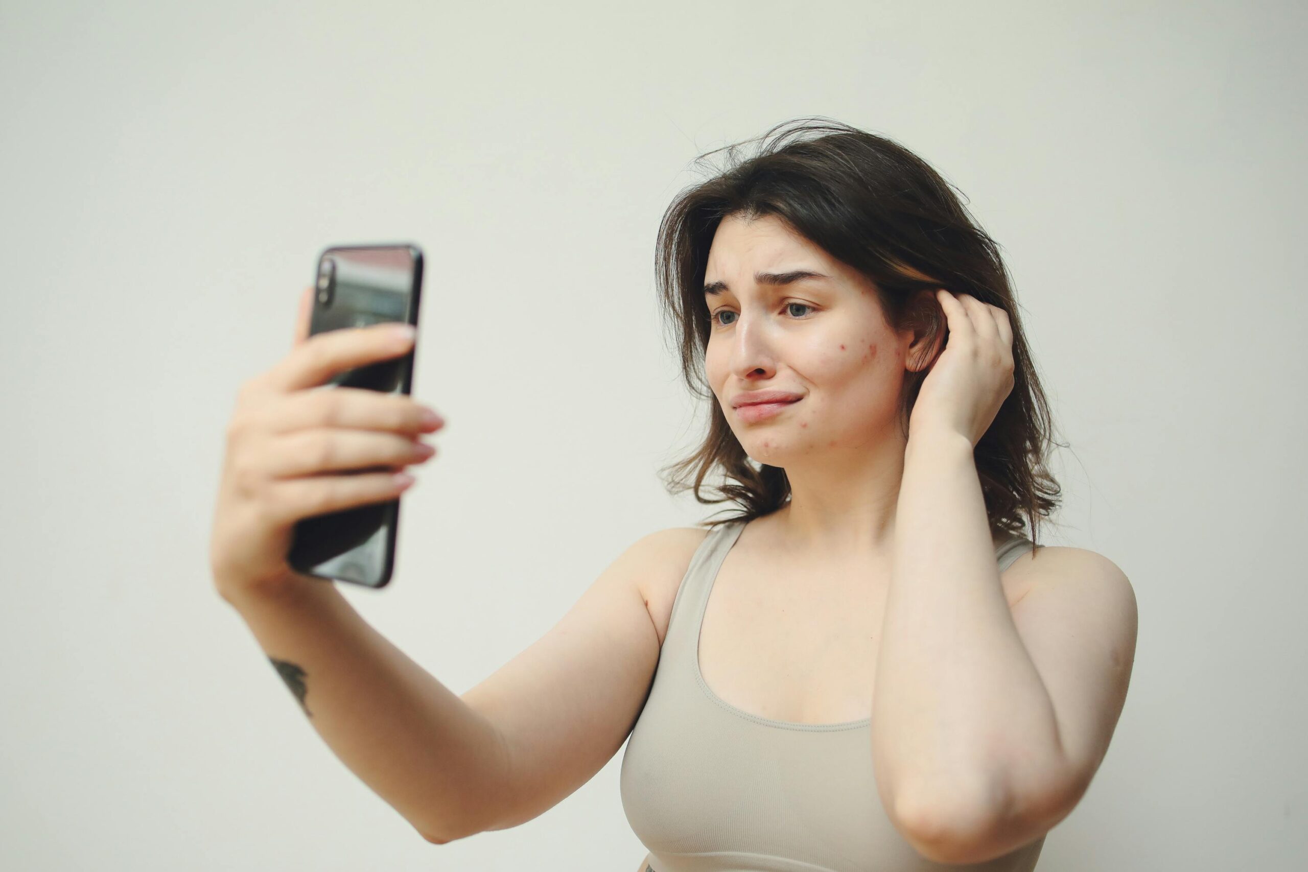 A young woman in a tank top taking a selfie with a worried expression on her face.
