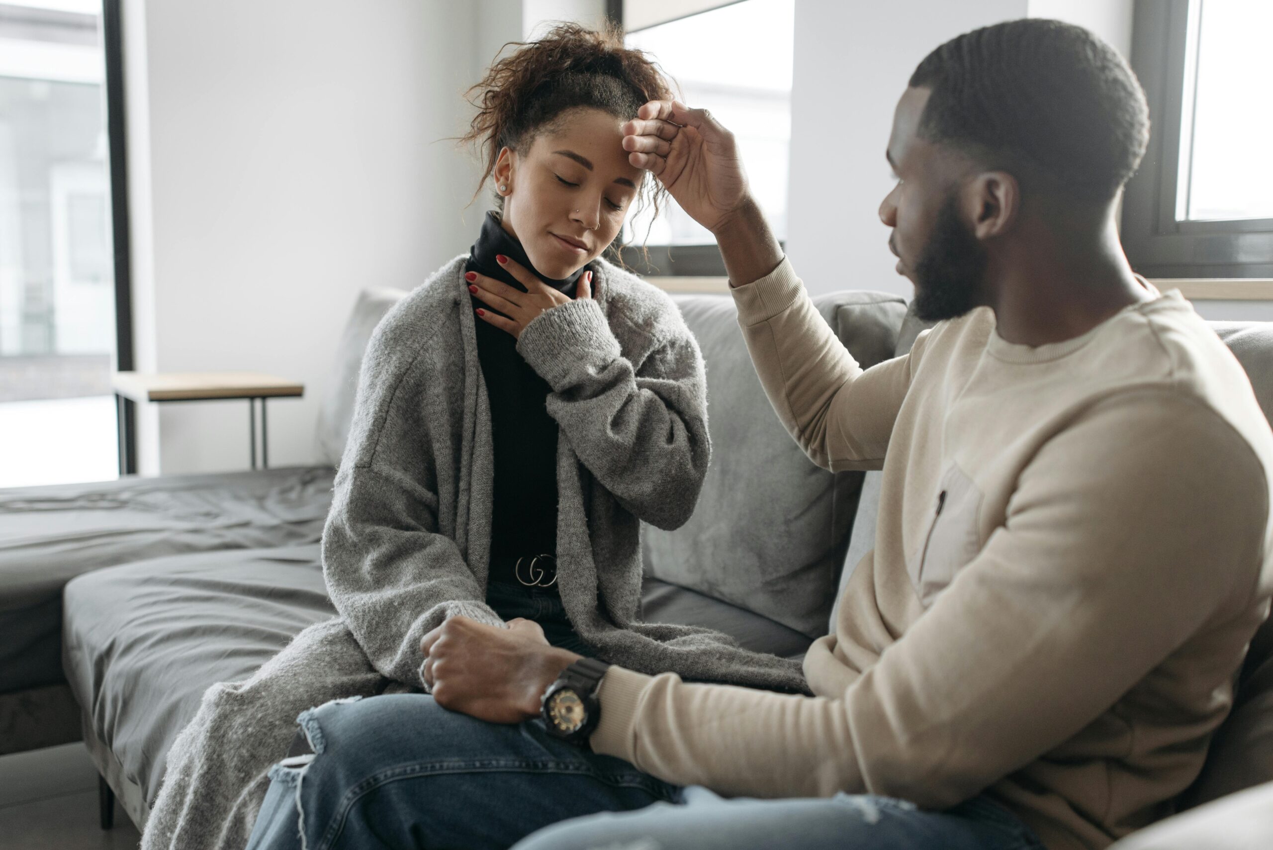 A concerned partner checks their sick loved one's fever while sitting on a sofa at home.