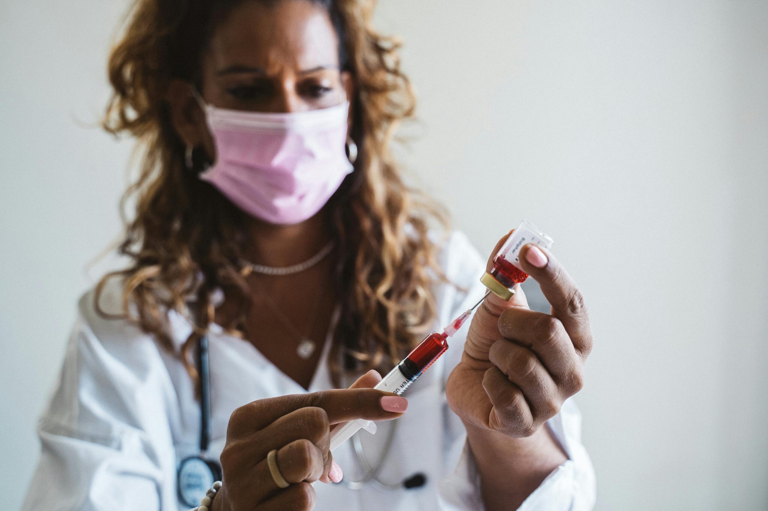 Medical professional wearing mask prepares syringe with vaccine in a healthcare setting.