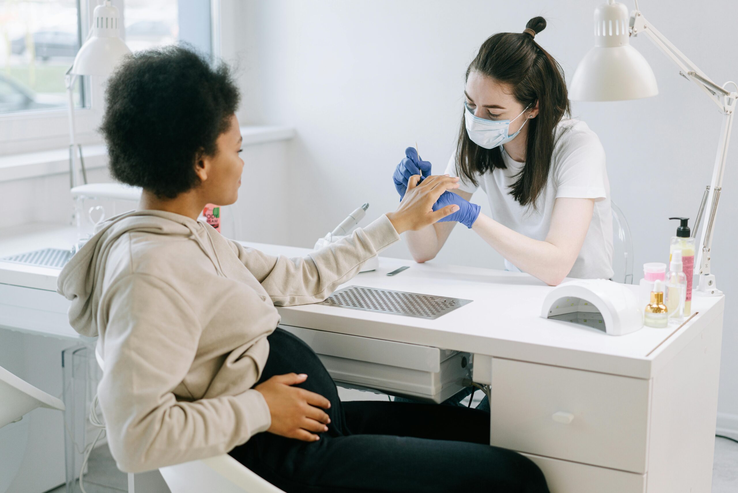 Pregnant woman at a nail salon receiving a manicure from a nail technician.