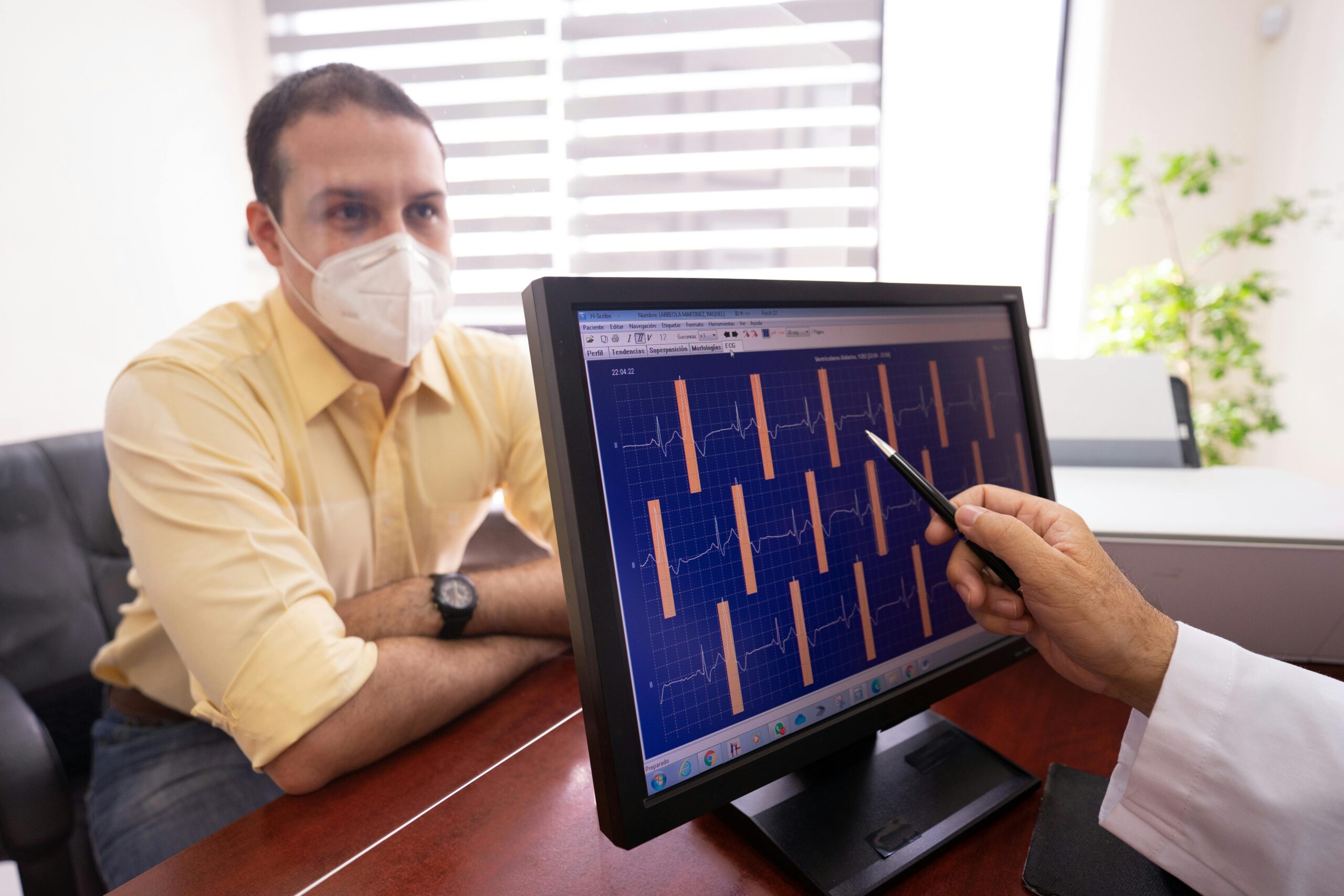 Medical consultation as a doctor reviews ECG results with a masked patient in a clinic setting.